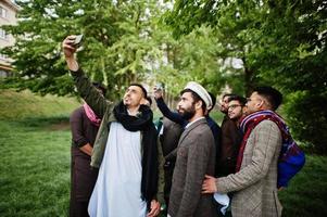 grupo de hombres paquistaníes vestidos con ropa tradicional salwar kameez o kurta haciendo selfie en el teléfono móvil. foto