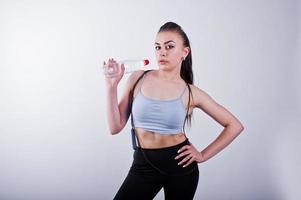 Cheerful attractive young fitness woman in top and black leggings with jump rope and bottle of water isolated over white background. photo