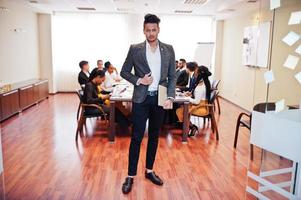 Face of handsome asian business man, holding laptop on the background of business peoples multiracial team meeting, sitting in office table. photo