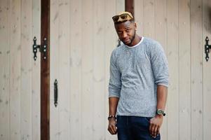 Stylish african american boy on gray sweater and black sunglasses posed on street. Fashionable black guy. photo