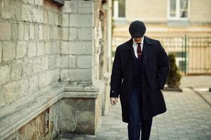 retrato de un hombre de negocios árabe inglés retro de los años 20 con abrigo oscuro, traje, corbata y gorra plana. foto