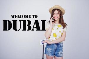 Girl tourist with bag, wear in shirt, shorts and hat, speaking on phone isolated on white. Welcome to Dubai. photo