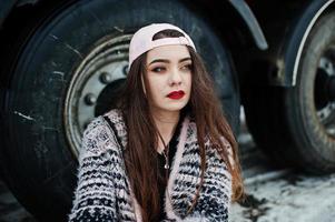 Brunette stylish casual girl in cap sitting against truck wheels. photo