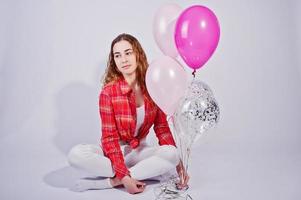 Young girl in red checked shirt and white pants with balloons against white background on studio. photo