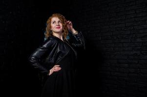 Curly hair girl at leather jacket on studio against black brick wall. photo