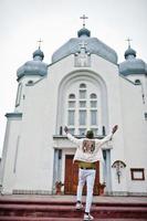 African american man in hat stand against church and put hands in air.  Faith and Christianity in Africa. photo