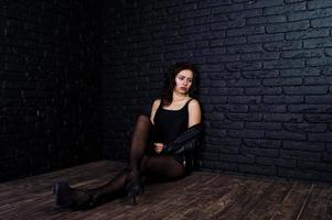 Studio portrait of sexy brunette girl in black leather jacket against brick wall. photo