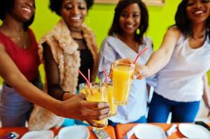 Four young african girls in bright colored pizza restaurant clinking juices. photo
