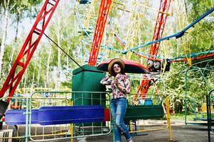 retrato de una chica morena con gafas rosas y sombrero con helado en el parque de atracciones. foto