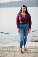 Pretty latino xxl model girl from Ecuador wear on violet blouse posed against lake. photo