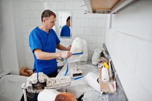 Prosthetist man making prosthetic leg while working in laboratory, makes a model of plaster. photo