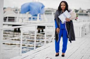 African american student girl in black graduation gown with diploma, at blue suit posed. photo