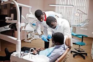 African american man patient in dental chair. Dentist office and doctor practice concept. Professional dentist helping his patient at dentistry medical. Drilling patient's teeth in clinic. photo