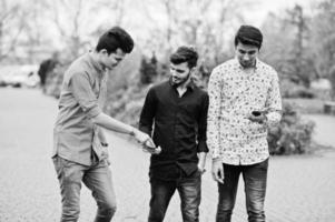 Three indian guys students friends walking on street and looking at mobile phone. Black and white photo. photo
