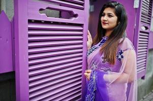 Indian hindu girl at traditional violet saree posed at street against purple windows. photo