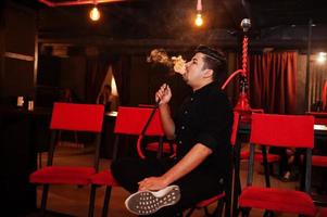 el hombre asiático fuma narguile y descansa en el bar salón. foto