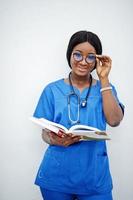 Portrait of happy female african american young doctor pediatrician in blue uniform coat and stethoscope with books at hands isolated on white. photo