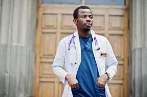 African american doctor male at lab coat with stethoscope outdoor against clinic door. photo