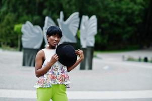 Amazing african american model woman in green pants and black hat posed at park. photo