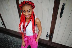 chica afroamericana de moda en pantalones rosas y rastas rojas posadas al aire libre. foto