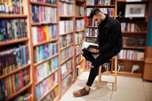 Tall smart arab student man, wear on black jeans jacket and eyeglasses, at library with book at hands. photo