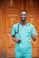 Portrait of African male doctor with stethoscope wearing green coat with mobile phone at hand. photo