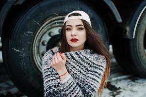 Brunette stylish casual girl in cap sitting against truck wheels. photo