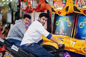 Two asian guys compete on speed rider arcade game motorcycle racing simulator machine. photo