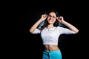 Portrait of an attractive young woman in white top and blue pants posing with her glasses in the dark. photo