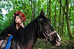 Mystical girl in wreath wear in black at horse in wood. photo