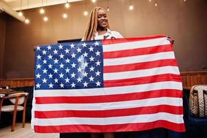 Beautiful african woman in stylish casual clothes posing with USA flag at hands in office. photo