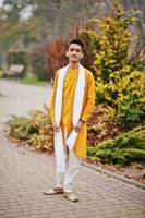 Indian stylish man in yellow traditional clothes with white scarf posed outdoor. photo