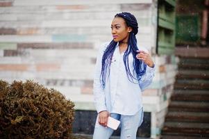 elegante chica afroamericana con rastas sosteniendo el teléfono móvil a mano, clima nevado al aire libre. foto