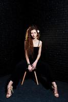 Studio shoot of girl in black on chair with dreads on brick background. photo