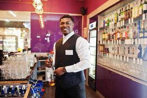 African american bartender at bar holding bootle. Alcoholic beverage preparation. photo