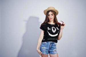 Portrait of an attractive girl in black t-shirt saying lol, denim shorts, hat and sunglasses posing in the studio. photo