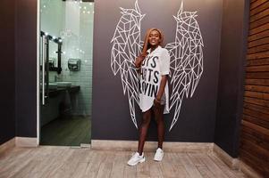 Beautiful african woman in stylish casual clothes posing against angel wings wall. photo
