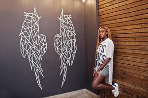 Beautiful african woman in stylish casual clothes posing against angel wings wall. photo