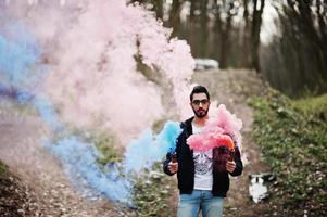 hombre árabe de estilo callejero con anteojos sostiene bengalas de mano con bomba de granada de humo rojo y azul. foto