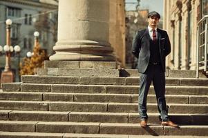 Portrait of retro 1920s english arabian business man wearing dark suit, tie and flat cap near old columns. photo