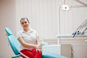 retrato de mujer dentista de pie en su oficina de odontología sentada en una silla. foto