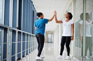 Two african woman friends in t-shirts give high five each other indoor together. photo