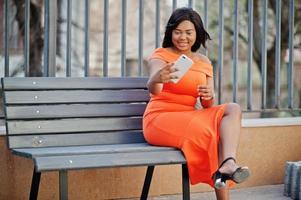 African american woman model xxl in orange dress looking on mobile phone. photo