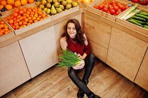 Girl in red holding green onions on fruits store. photo