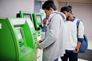 dos chicos asiáticos sacan dinero en efectivo de un cajero automático verde. foto