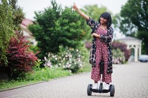 hermosa mujer afroamericana usando segway o hoverboard. chica negra en scooter eléctrico autoequilibrado de doble rueda. foto