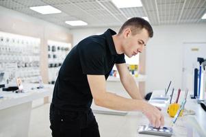 vendedor hombre consultor profesional de telefonía móvil en tienda de tecnología o tienda tiene un nuevo teléfono inteligente a mano. foto