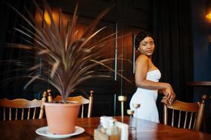 African american woman, retro hairstyle in white dress at restaurant. photo