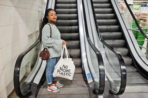 mujer africana con bolsas ecológicas de compras en escaleras mecánicas en el centro comercial. foto