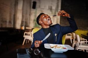 Fashionable african american man in suit sitting at cafe and eating salad. photo